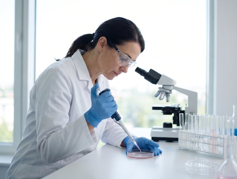 Una ricercatrice in laboratorio con guanti blu esamina cellule in una piastra